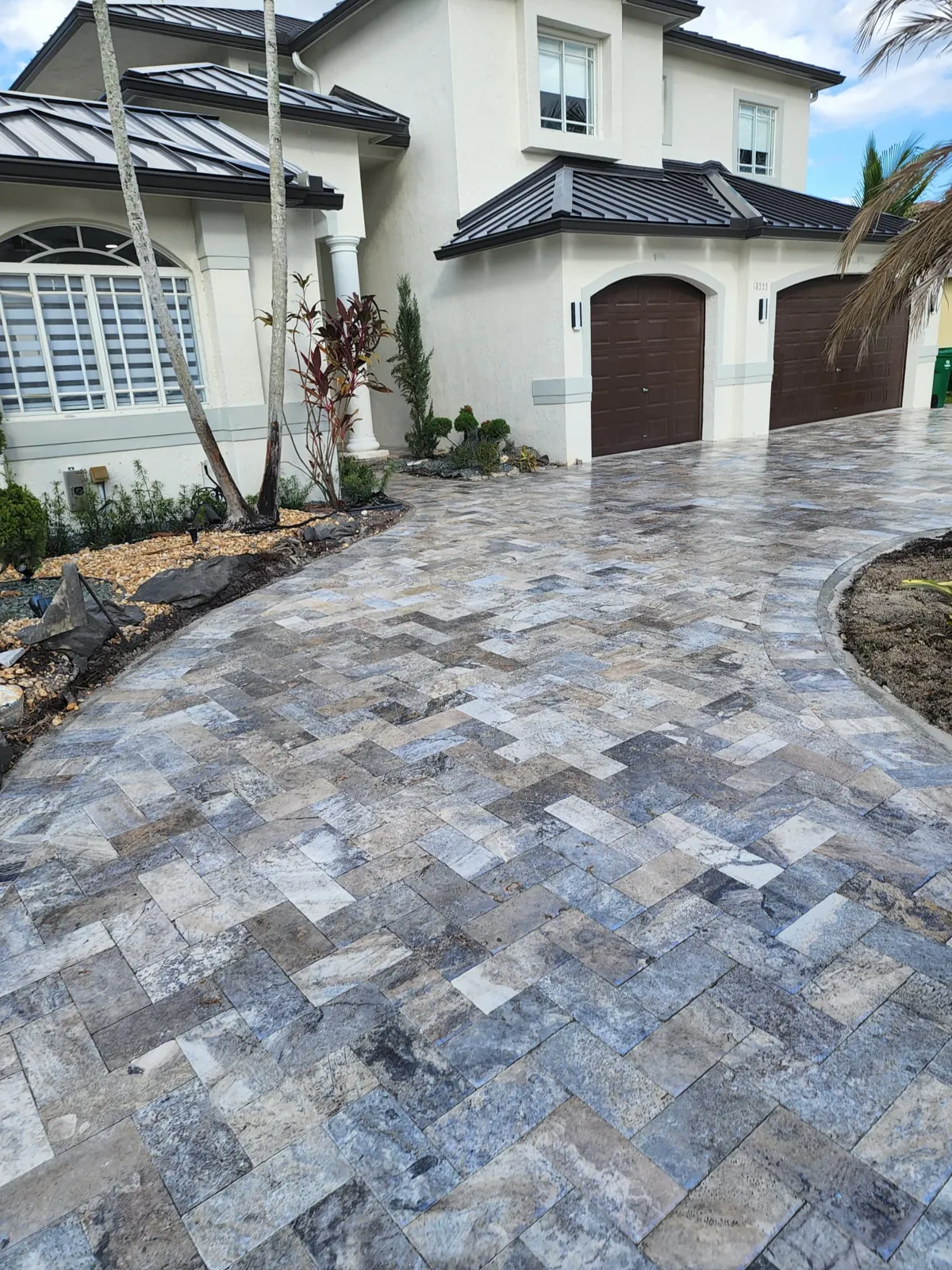 Patterned silver-gray stone pavers on a driveway leading to arched garage doors