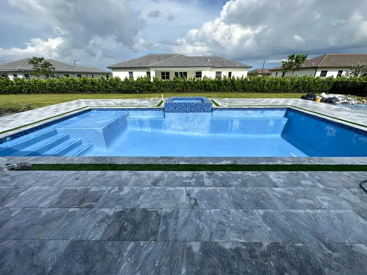 Dark gray stone surround and a blue pool with a raised spa wall