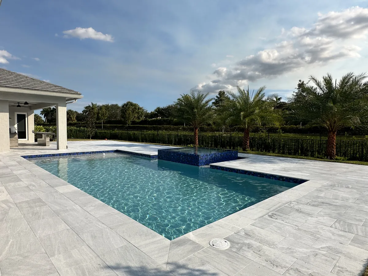 Pale veined paving around a rectangular pool with a raised spa beside a covered patio
