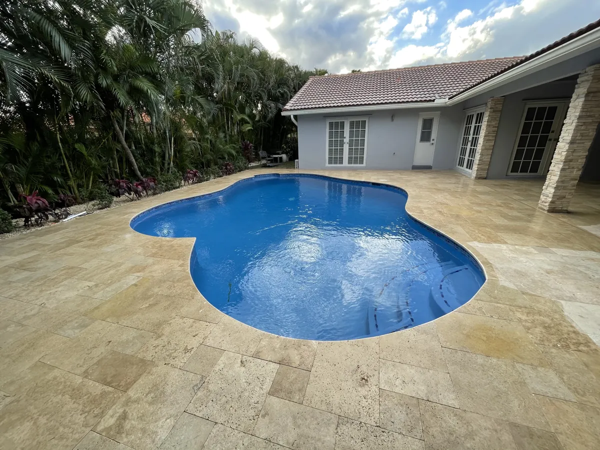 Freeform pool surrounded by warm travertine-toned paving