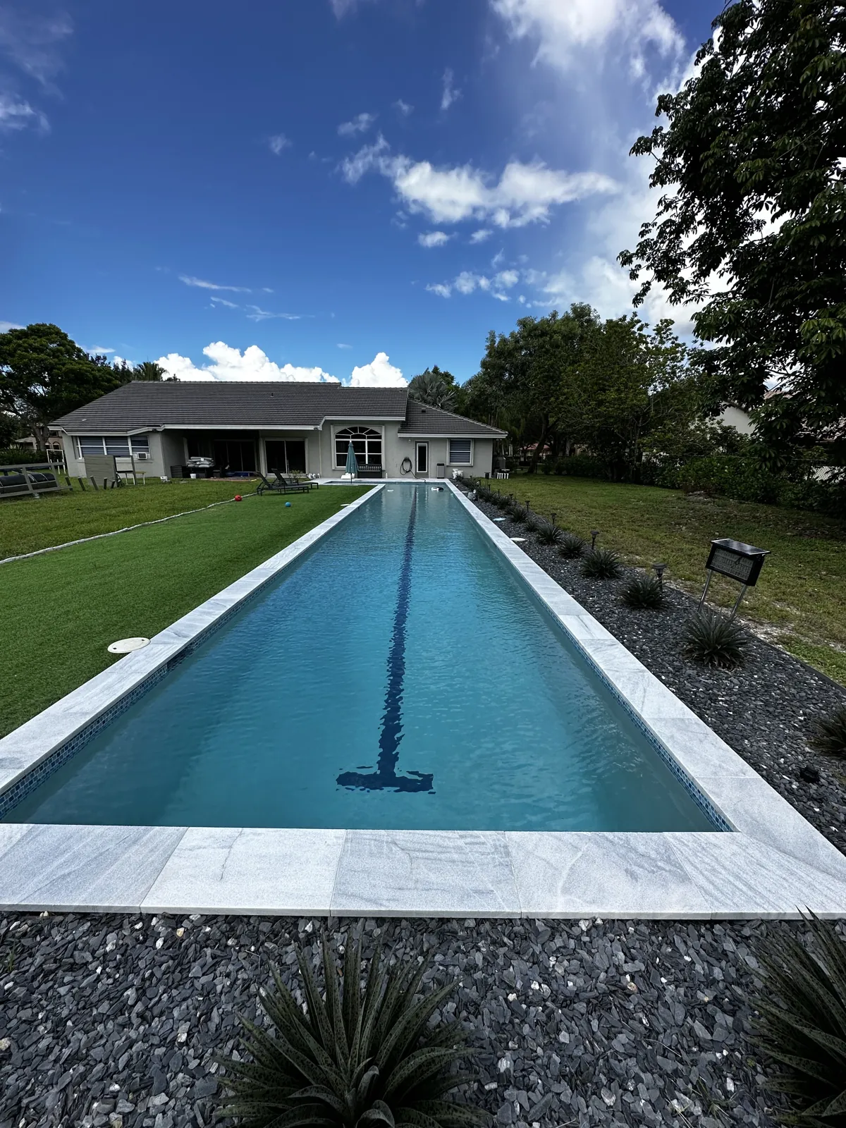Narrow lap-style pool with pale coping and dark landscape stone along the edge