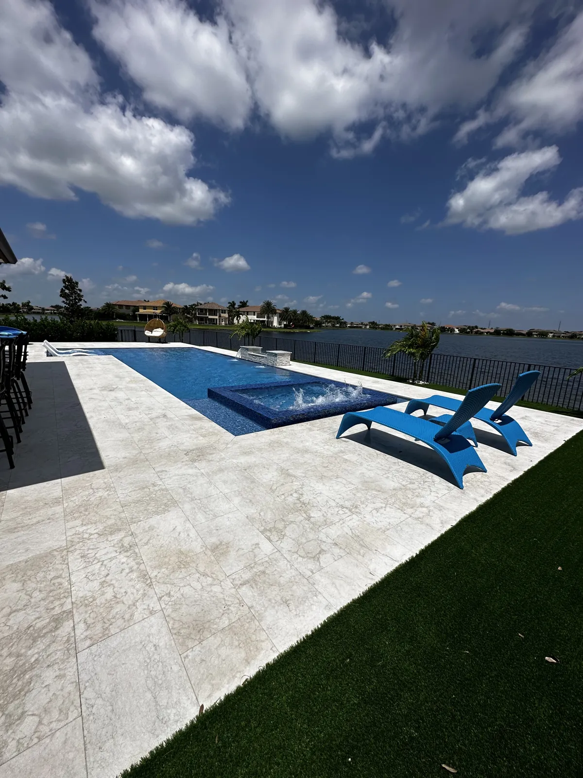 Pool with a lounge shelf, turf edge and pale stone deck beside a dark fence
