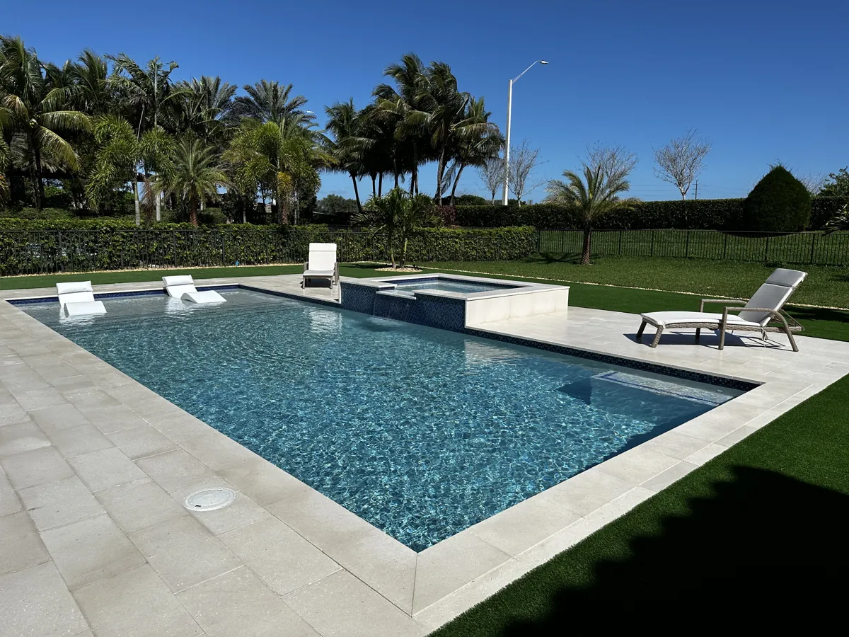 Pool with in-water lounge shelves, a raised spa and pale stone coping beside turf