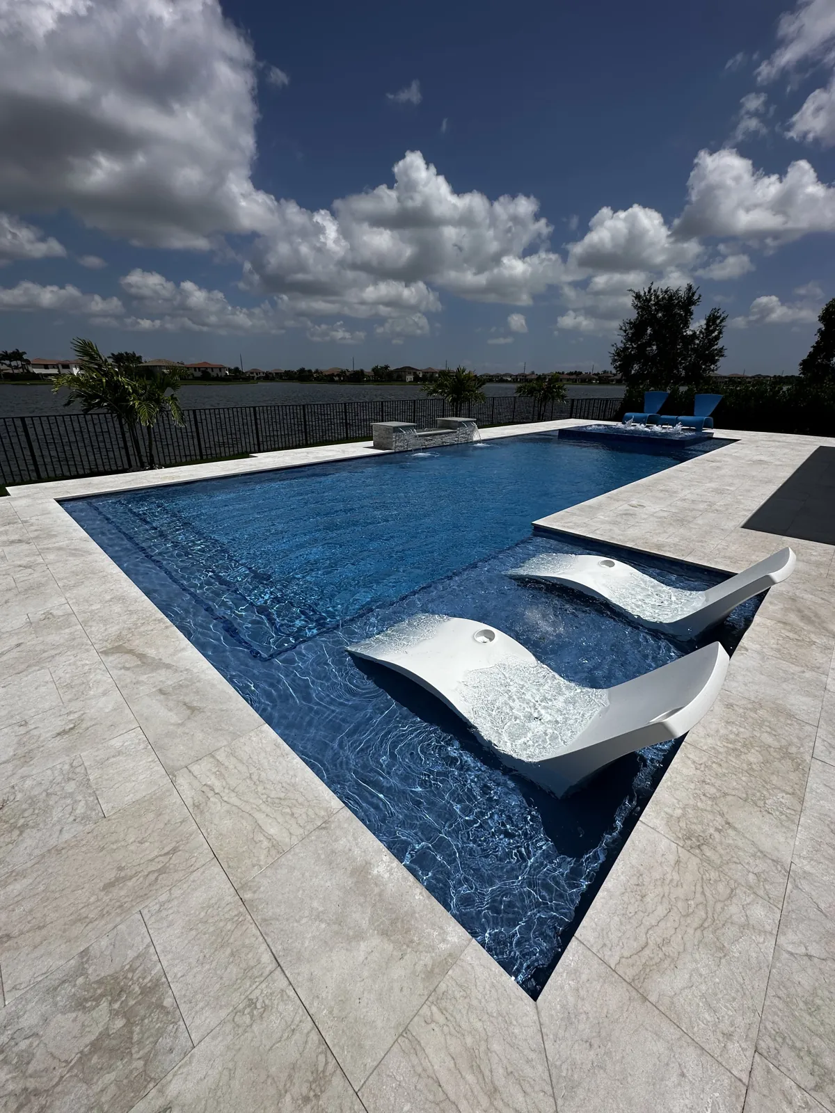 Pool lounge shelves framed by pale stone paving under a blue sky