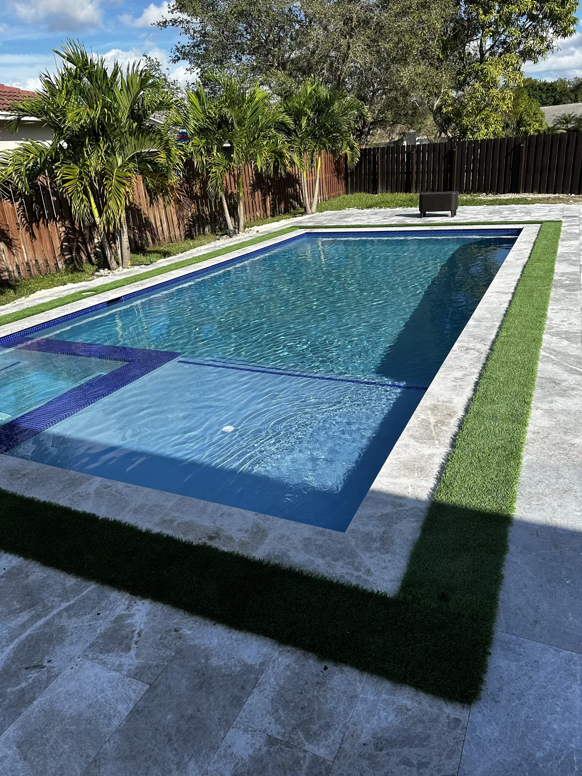 Pool bordered by a cream coping band and a turf strip over pale stone paving